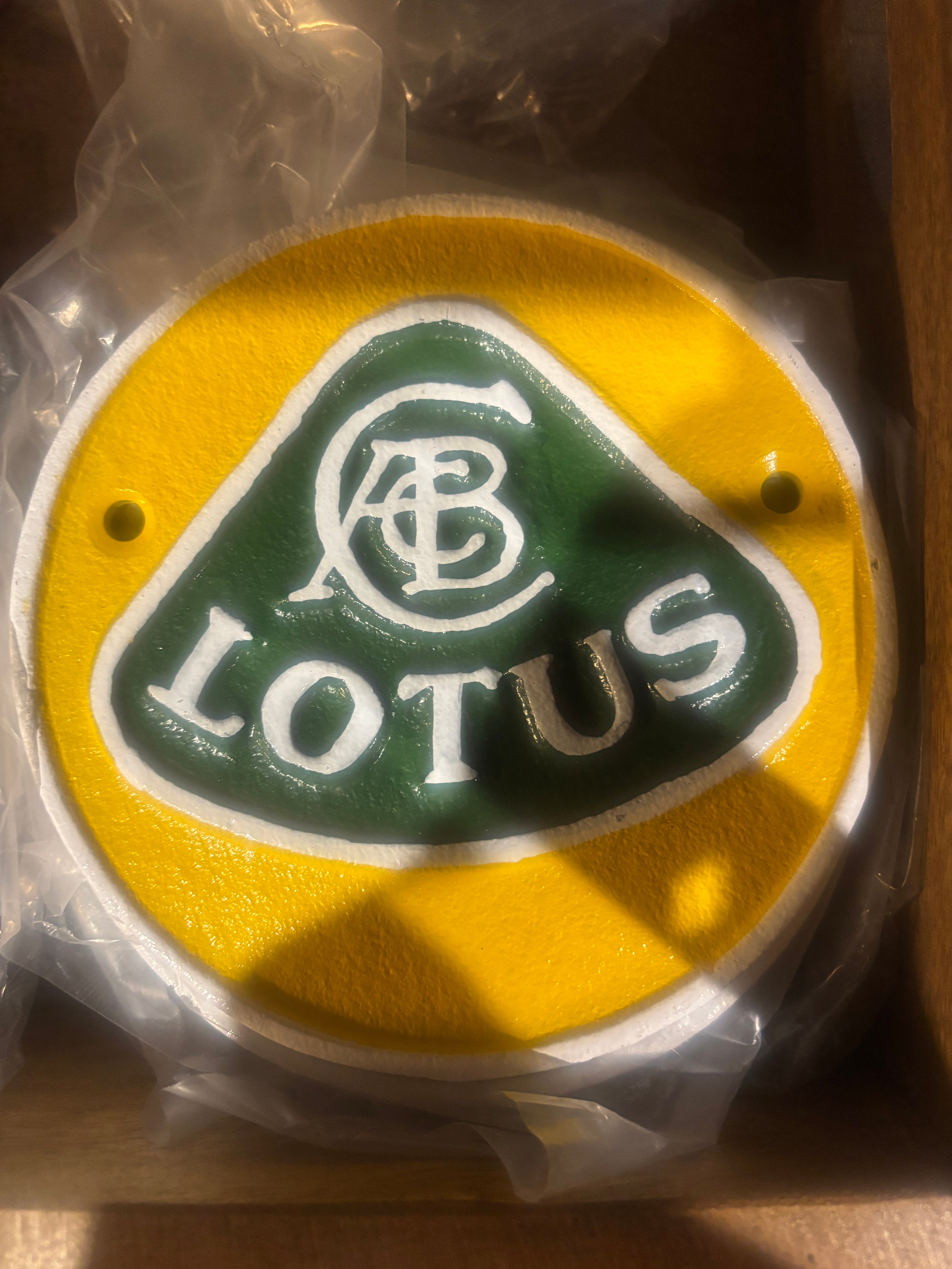 Lotus logo on a yellow background cast metal plaque, still in packaging