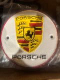 Porsche logo on a round, white background with red and yellow accents cast metal plaque.