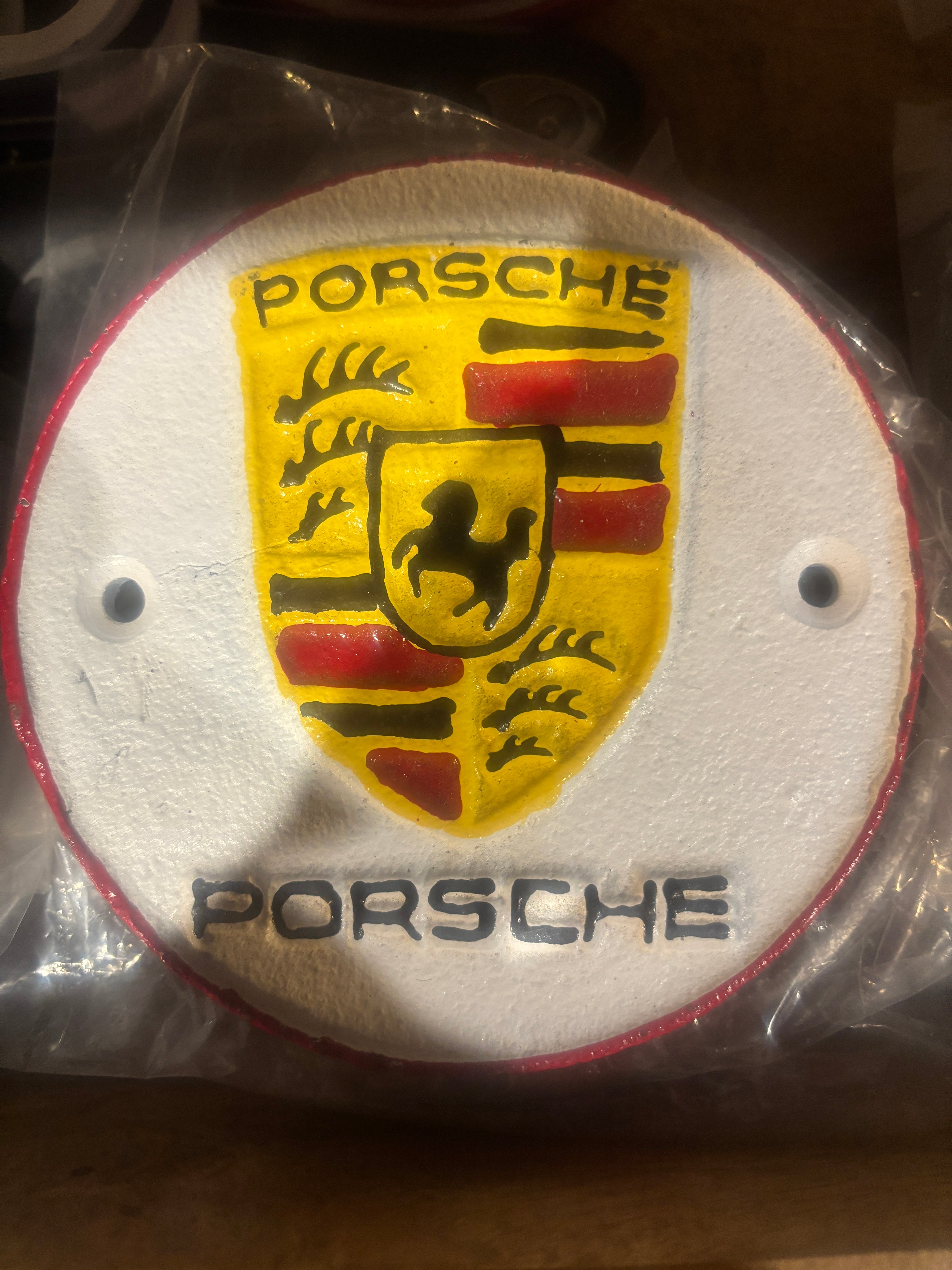 Porsche logo on a round, white background with red and yellow accents cast metal plaque.