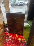 Wooden chest of drawers with gold handles on a red patterned rug.